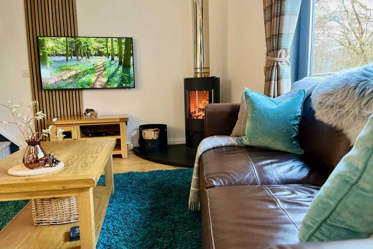 The cosy lounge with wood-burning stive and glass picture windows at Bluebell Cottage Glencoe.
